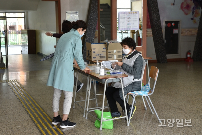 투표소 입구에서 유권자들이 발열체크, 손소독, 일회용 비닐장갑을 착용하고 입장하고 있다.